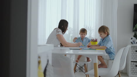 Two-children-of-boys-draw-with-his-mother-sitting-in-the-kitchen.-Happy-family-at-home.